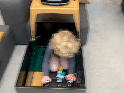 Shows a little girl sitting in the racing simulator pressing the pedals with her hands